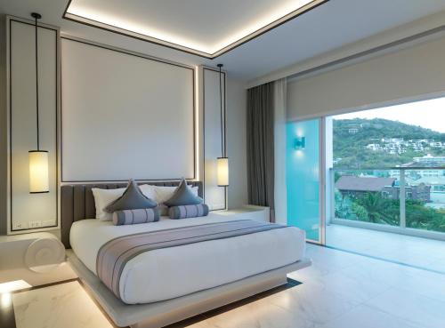a bedroom with a white bed with a large window at Chanalai Romantica Resort - Adults Only, Kata Beach in Kata Beach