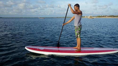 a man standing on a paddle board in the water at The Majlis Resort in Lamu