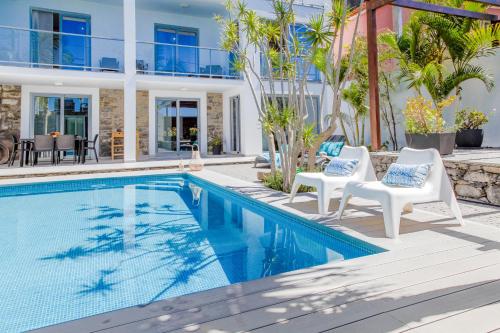 una piscina con 2 sillas blancas y una casa en Madeira Beach House - by LovelyStay, en Madalena do Mar