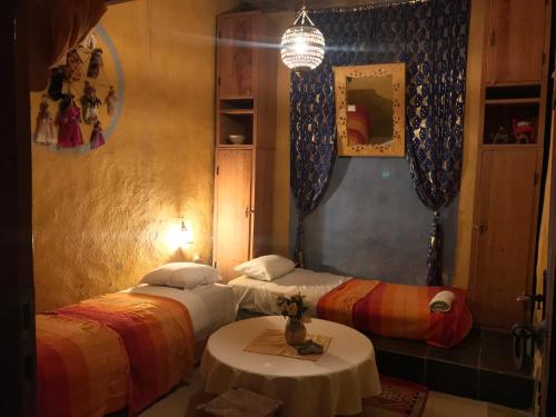 two beds in a room with a table and a lamp at Auberge Chez Julia in Merzouga