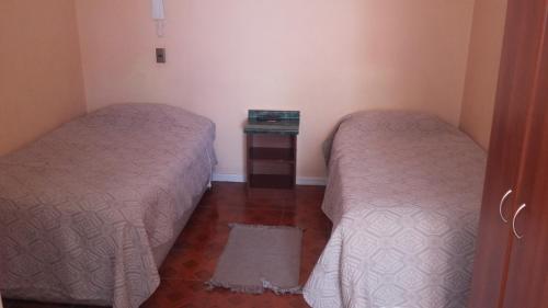 two beds in a room with a small table between them at Hotel Don Alfredo in Calama