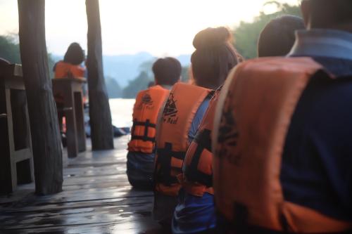 a group of people in orange life vests sitting on a dock at The For Rest Resort in Sai Yok
