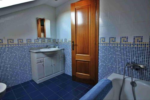W wyłożonej niebieskimi kafelkami łazience znajduje się umywalka i wanna. w obiekcie Casa de O Rosal w mieście San Bartolomé