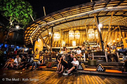 a group of people sitting on benches in front of a building at The Mud - Eco Hotel in Ban Bang Po