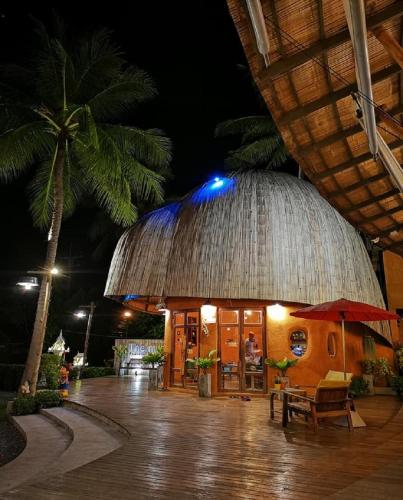 a building with a straw roof with a table and a umbrella at The Mud - Eco Hotel in Ban Bang Po