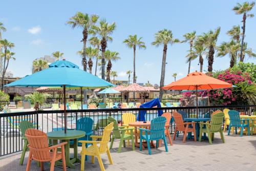 a group of tables and chairs with umbrellas and palm trees at Isla Grand Beach Resort in South Padre Island