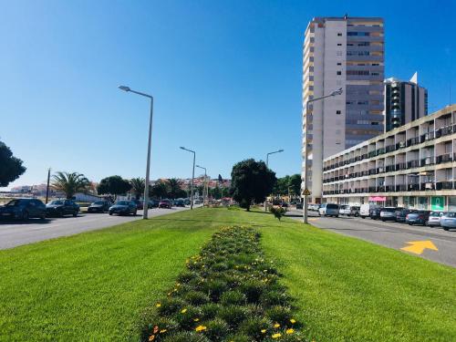 a field of grass next to a street with a building at Sabor a Verão, T1 em frente à praia com TV in Figueira da Foz