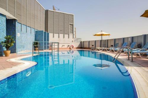 duży niebieski basen z krzesłami i parasolem w obiekcie Pearl Executive Hotel Apartments w Dubaju