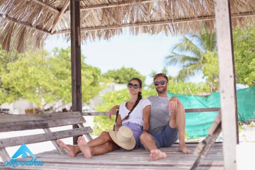 Un uomo e una donna seduti su una panchina sulla spiaggia di Moodhu Surf House a Himmafushi