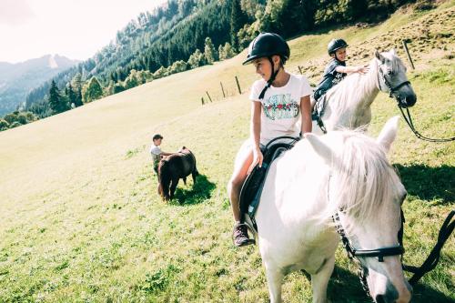 two children are riding on horses in a field at Kinderhotel Stegerhof in Donnersbachwald