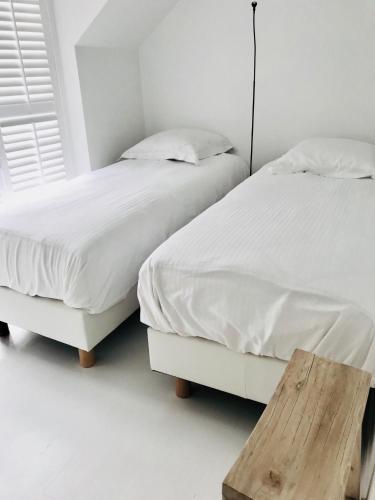 two beds with white sheets and a wooden bench in a bedroom at LivingTheMoment in Ghent