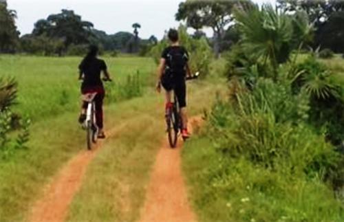 two people riding bikes down a dirt road at The Backwaters Lodge in Wilpattu