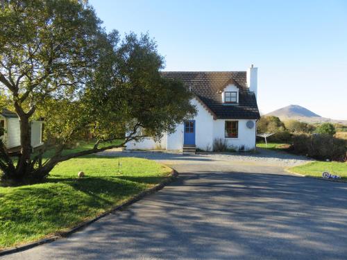 a white house with a tree and a road at Letterfrack Farm Cottage in village on a farm beside Connemara National Park in Letterfrack