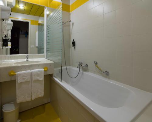 a bathroom with a tub and a sink and a mirror at Hôtel des Mosaiques in Orbe
