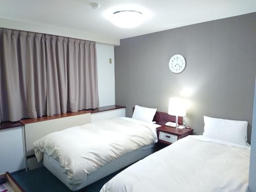 2 camas en una habitación con un reloj en la pared en Hotel Crown Hills Imabari en Imabari