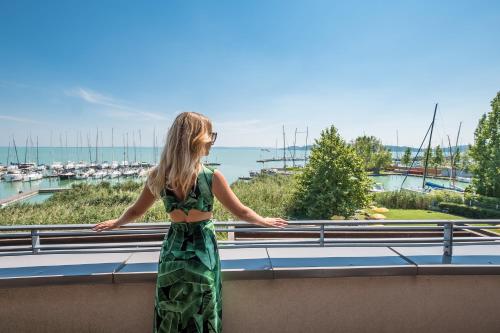 a woman standing on a balcony looking out at the harbor at Hotel Golden Lake Resort in Balatonfüred