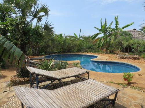 two wooden benches sitting next to a swimming pool at Bahati Diani House Glamping in Diani Beach