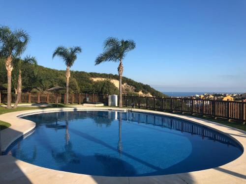 einen Pool mit Palmen und dem Meer im Hintergrund in der Unterkunft Alcaidesa Golf & Relax in Alcaidesa
