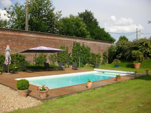 a swimming pool with a wooden deck and an umbrella at Château de Cleuville in Cleuville