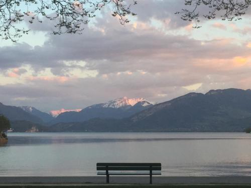 a bench sitting in front of a lake with mountains at The One Suite Annecy in Annecy