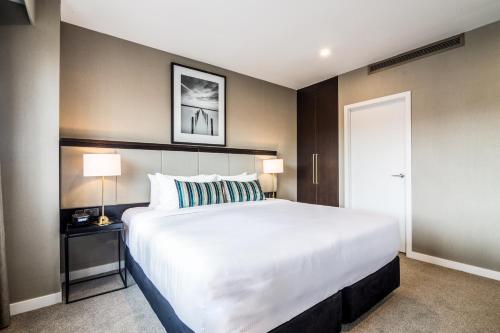 a bedroom with a large white bed and two lamps at The Sebel Auckland Manukau in Auckland