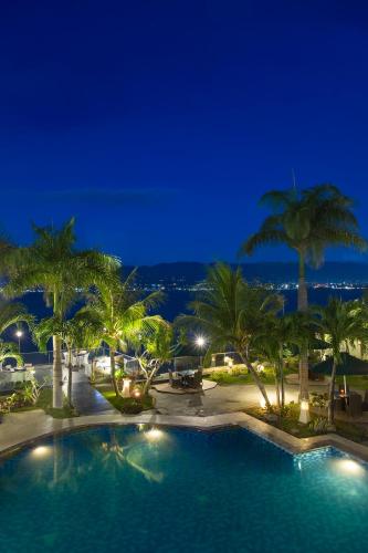 a large swimming pool with palm trees at night at Swiss-Belhotel Silae Palu in Palu