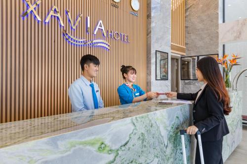 a woman standing at a counter talking to two people at Xavia Hotel in Nha Trang