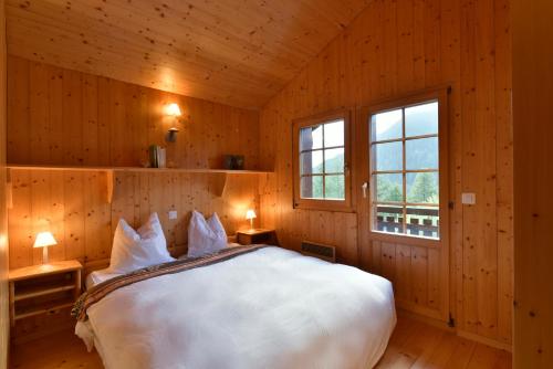 グリメンツにあるChalet Freschの木製の部屋に白い大型ベッドが備わるベッドルーム1室
