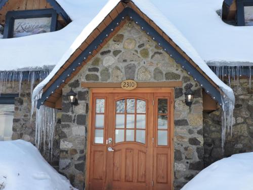 a stone cottage with a wooden door in the snow at Auberge Spa & Beaux Reves in Sainte-Adèle