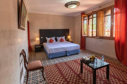 a bedroom with a bed and a table and windows at Hôtel Riad Airport Marrakech in Marrakech