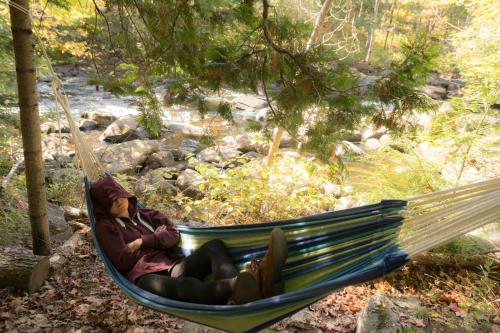 a woman sitting in a hammock next to a river at Auberge Spa & Beaux Reves in Sainte-Adèle
