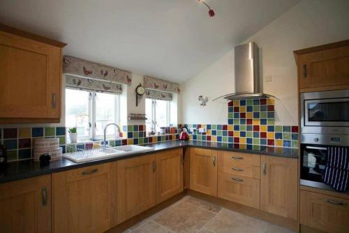 a kitchen with wooden cabinets and colorful tiles on the wall at Squeak Cottage in Harrogate