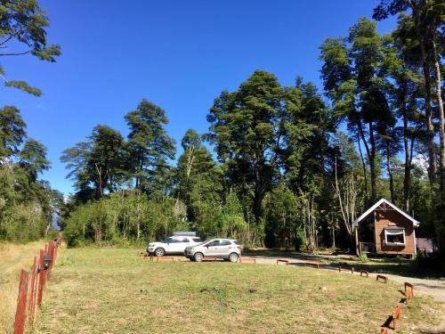 two cars parked in a field next to a cabin at Cabañas Nutrias Patagonicas in Puelo