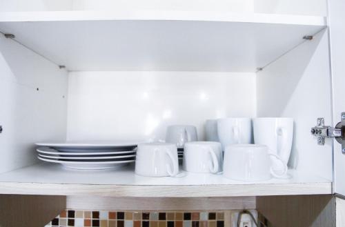 a shelf with white cups and plates on it at Pool View 2BR Mutiara Bekasi Apartment By Travelio in Bekasi