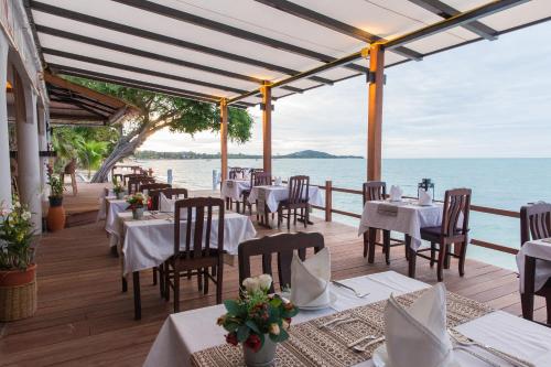 a restaurant with white tables and chairs and the ocean at Adarin Beach Resort in Mae Nam