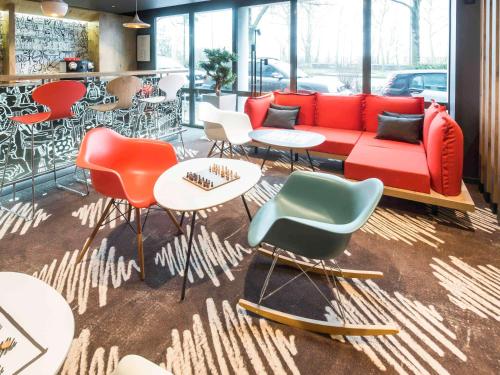 ibis Rouen Centre Champ de Mars في رووين: غرفة بها أريكة حمراء وكراسي وطاولات