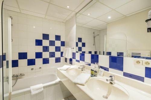 La salle de bains est pourvue d'un lavabo, d'une baignoire et d'un miroir. dans l'établissement Hotel Kempense Meren by Sunparks, à Mol
