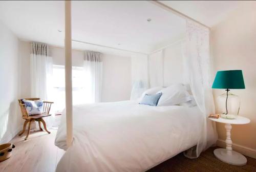 Dormitorio blanco con cama blanca con dosel y lámpara verde en The Boat House en Aldeburgh