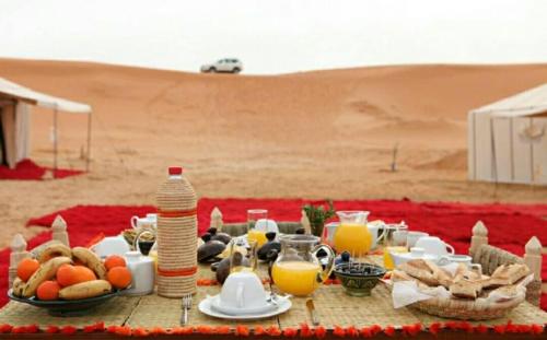 una mesa con comida y bebidas en el desierto en Erg Lihoudi Dunes & Bivouac, en Mhamid