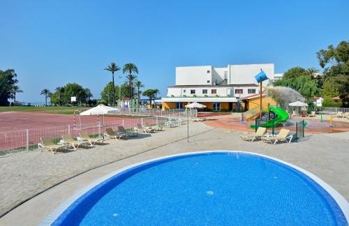 a swimming pool with chairs and umbrellas and a tennis court at Sol Marbella Estepona Atalaya Park in Estepona