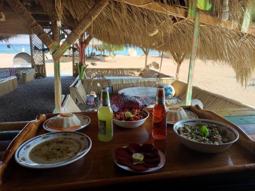 una mesa de madera con platos de comida y bebida en la playa en SakraTah Camp - eco friendly, en Taba