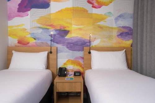 two beds in a room with a colorful wall at Ibis Styles Hobart in Hobart