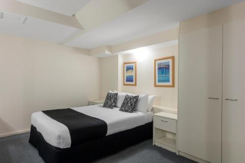 a white bedroom with a bed and a cabinet at Nesuto The Entrance in The Entrance