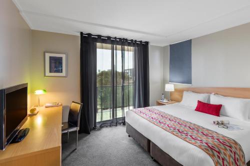 a hotel room with a bed and a desk and a television at Nesuto Parramatta in Sydney