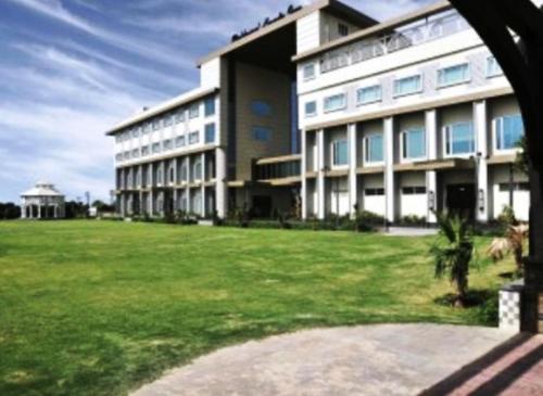 a large building with a grass field in front of it at Brijwasi Lands Inn in Mathura