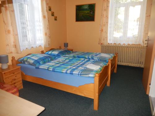 a bedroom with a wooden bed with a blue comforter and two windows at PENZION MANĚTÍN u Sv. Barbory in Manětín