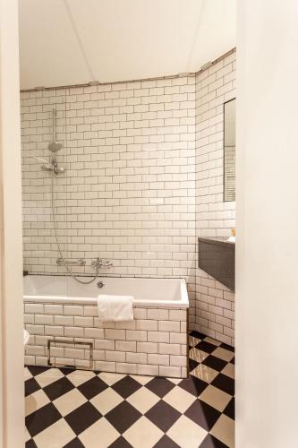a white tiled bathroom with a tub and a sink at Avenue Hotel by F-Hotels in Blankenberge