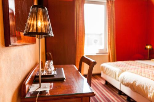 Cette chambre d'hôtel comprend un bureau avec une lampe et un lit. dans l'établissement Malecot Hotel by F-Hotels, à Blankenberge