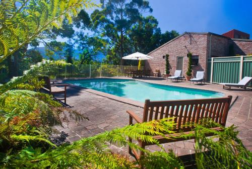 a swimming pool with two benches and an umbrella at The Shingles Riverside Cottages in New Norfolk