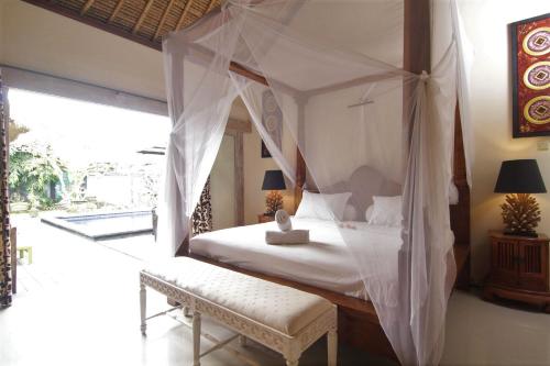a bedroom with a canopy bed and a bench at Bamboo Moon Villas in Sanur